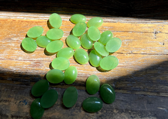 Group of light green Canadian jade cabochons 10x14mm scattered on a weathered wooden surface