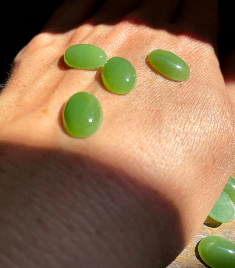 Several light green Canadian jade cabochons on a sunlit hand with shadows
