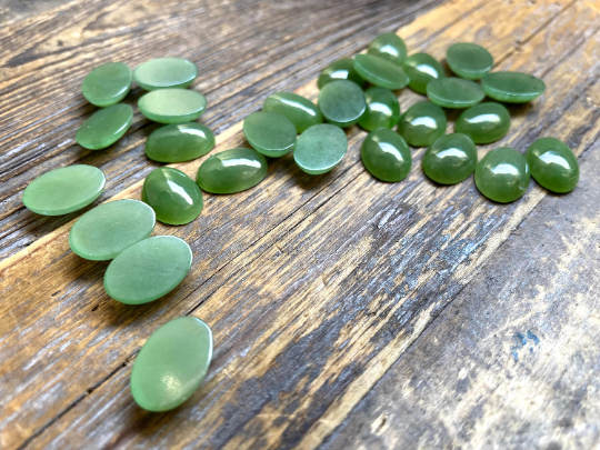Light green Canadian jade cabochons in oval shapes scattered on a rustic wooden surface