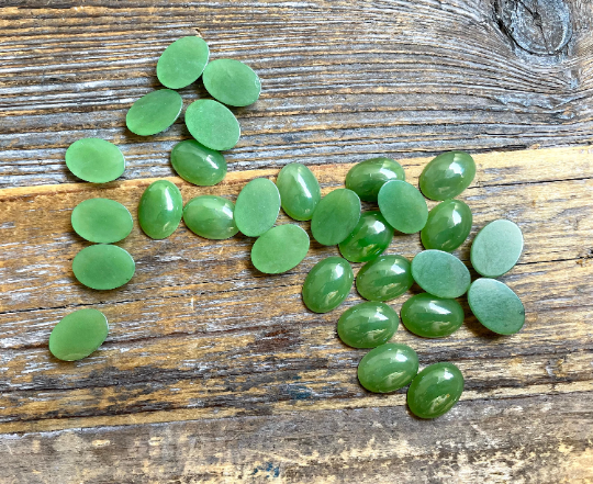 Light green Canadian jade cabochons in oval shapes spread across a weathered wooden surface