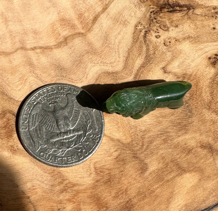 Small green jade lion figurine next to a quarter for scale on a wooden surface