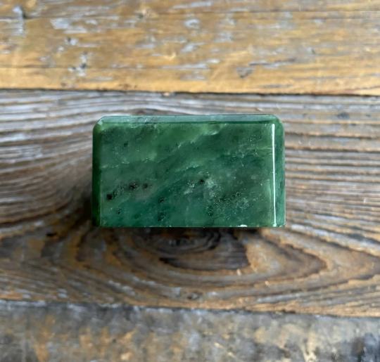 Emerald-green rectangular mineral sample photographed from above on a rustic wooden surface.