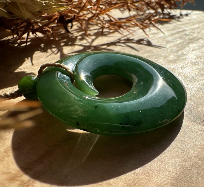 Donut shaped green jade pendant with central hole on a brown braided cord