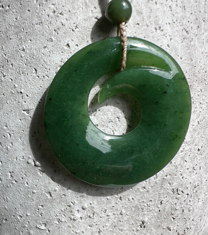 Green jade donut pendant with an inner crescent cutout suspended by a cord