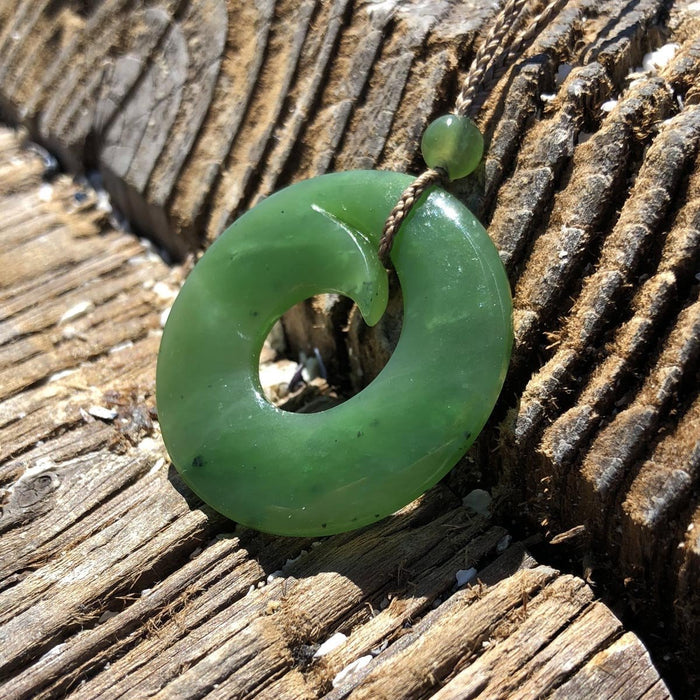 Green jade donut pendant on a braided cord with a small bead, shown on weathered wood.