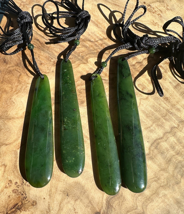 Four long jade pendant drops on black cords with knotted loops