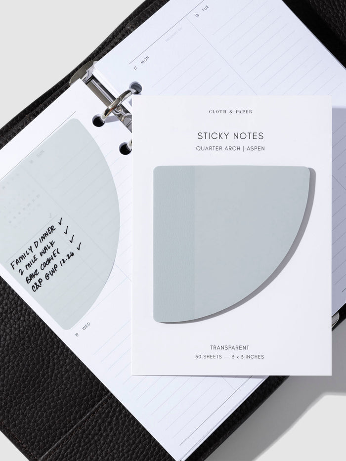 Sticky note in use inside a black leather planner. It is written on with a black oil based ink pen. The other sticky notes are displayed on top of it on their backing.