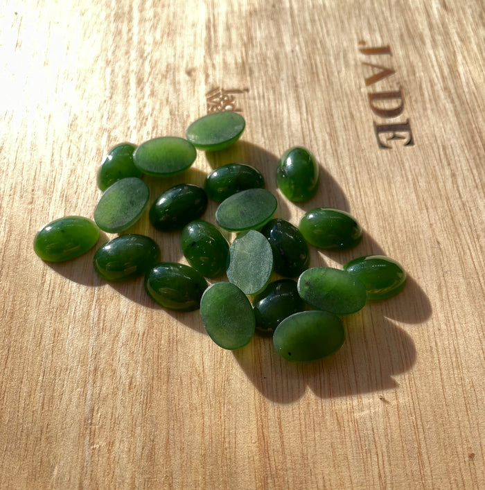 14x10mm rich green oval Siberian jade cabochons on a wooden surface