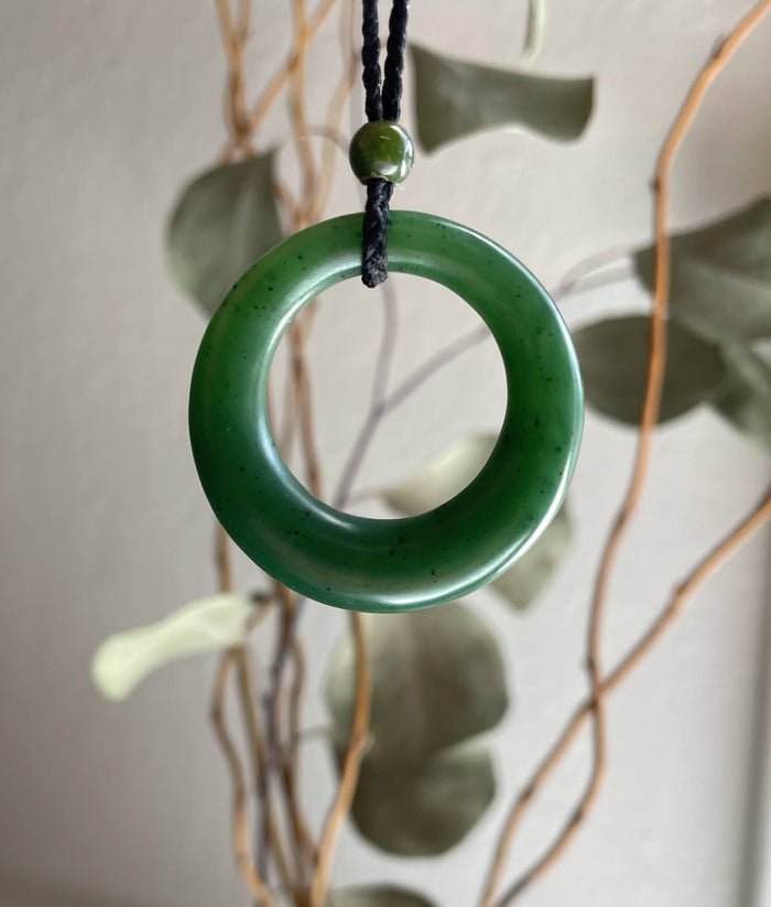 Round jade pendant on black braided cord with a small green bead above.