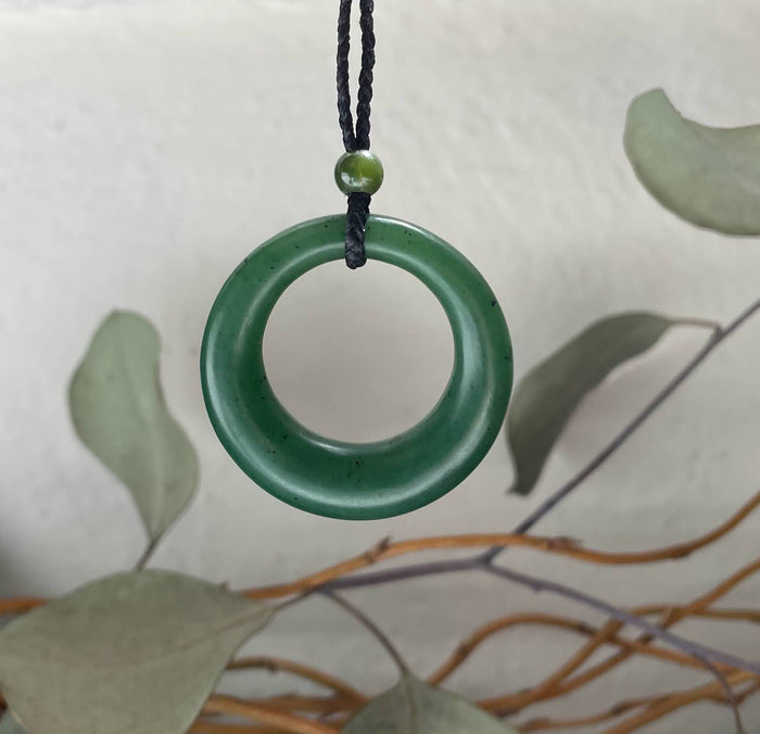 Round jade donut pendant on a black cord with a small green bead above against a light background.