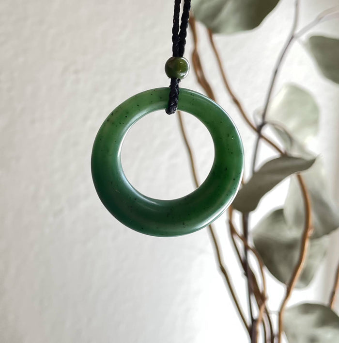 Close up of round jade donut pendant suspended from a black cord with a bead above.
