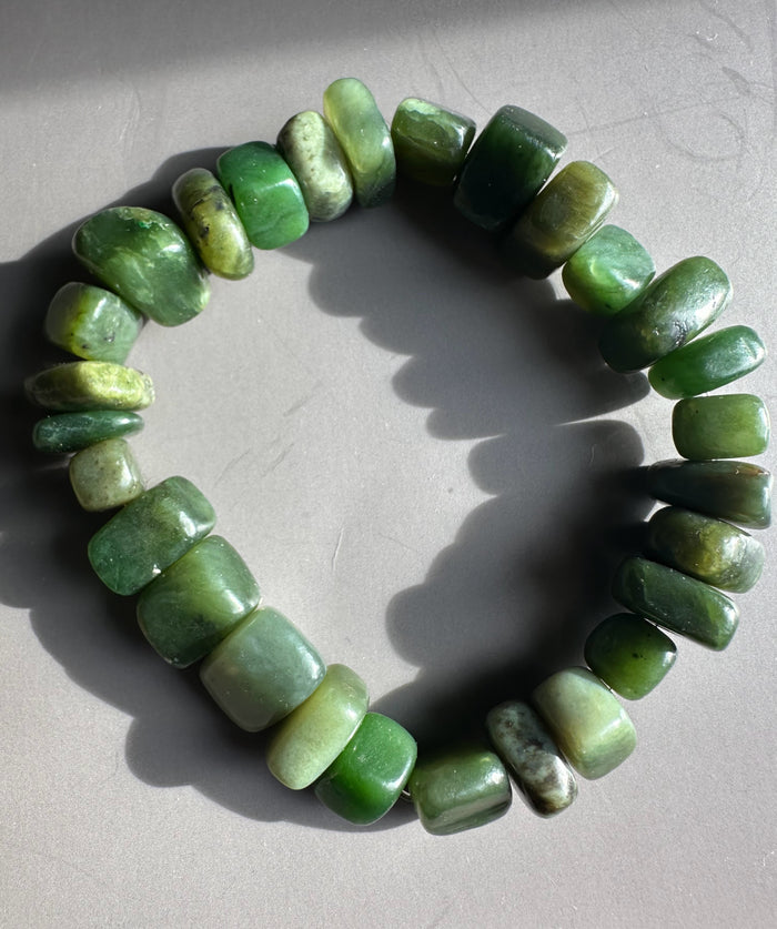 Satin finish green nugget bracelet laid in a circle on a light gray surface