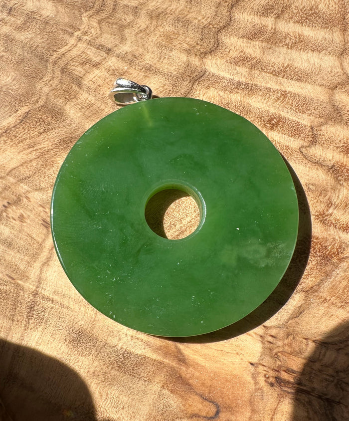 Siberian Jade Disc 40mm pendant with silver bail resting on a brown textured surface.
