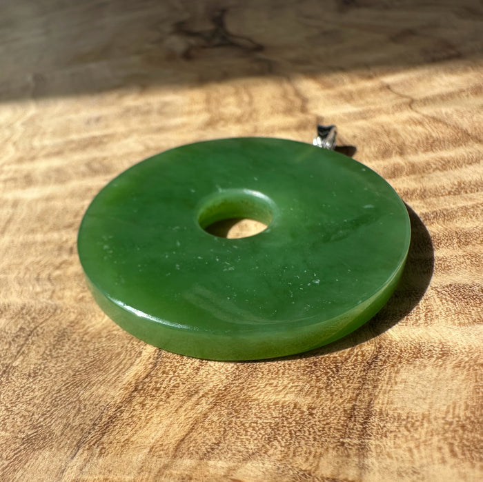Siberian Jade Disc 40mm pendant with silver bail on a silver chain hanging in a dim indoor setting.