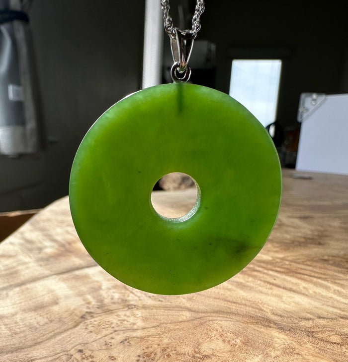 Siberian Jade Disc 40mm pendant with bail and chain against a bright indoor background.