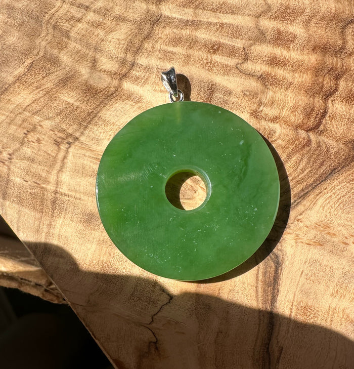 Siberian Jade Disc pendant 40mm in glossy green with a silver bail on a textured brown surface.