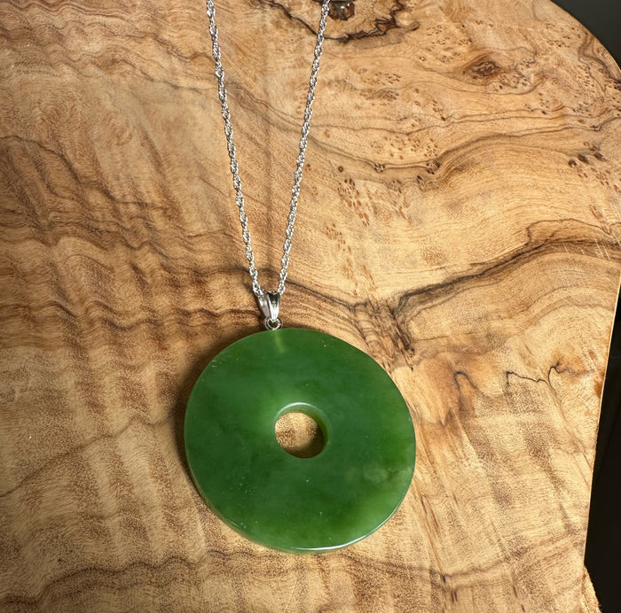 40mm Siberian Jade Disc pendant with silver chain resting on a wood grain surface.