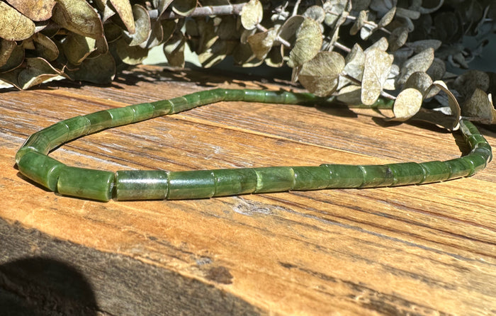 Green Siberian Jade tube bead necklace resting on a rustic wooden surface.