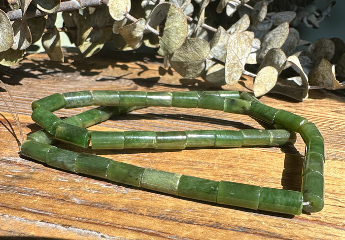 Two strands of green Siberian Jade tube beads spread on a wooden table.