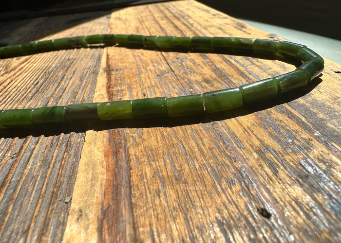 18 inch strand of glossy green jade tube beads resting on a sunlit wooden surface