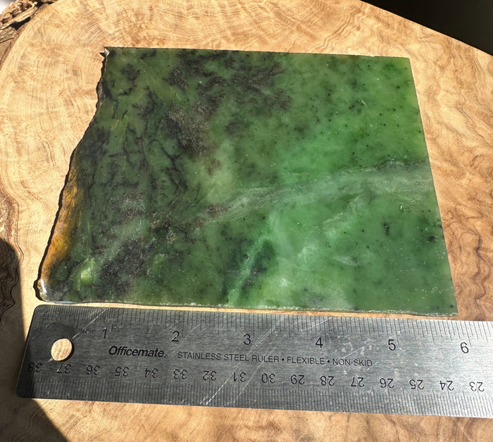 A rectangular green stone slab with natural marbling and rough edges, placed on a wooden surface with a metal ruler below it for scale.