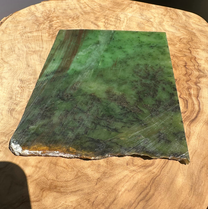 A raw green stone slab with natural marbling and rough edges, displayed on a light-colored wooden surface.