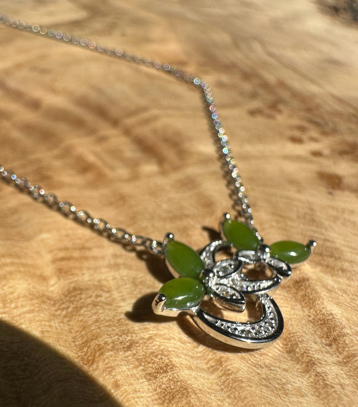 Close-up of silver butterfly pendant with green marquise stones and crystal accents on a chain.