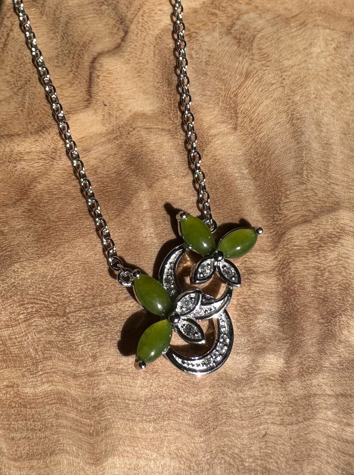 Detailed view of silver butterfly pendant featuring green stones and crystal accents on a wooden surface.