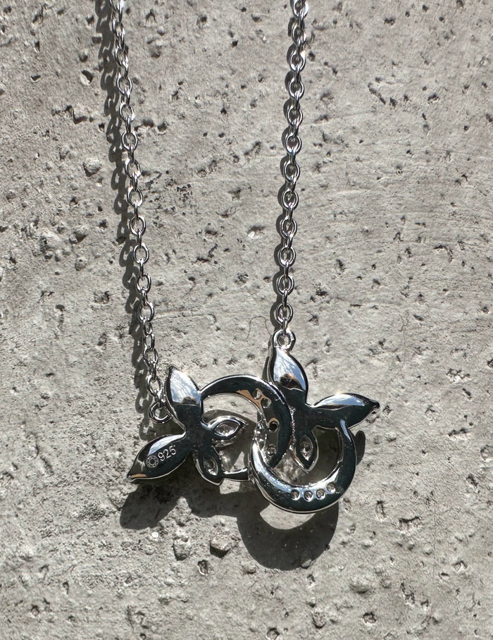 Back view of silver butterfly pendant showing 925 stamp and hollow decorative design against a stone surface.