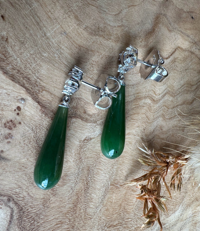 Silver drop earrings with green teardrop stones and ornate silver tops on a wood surface