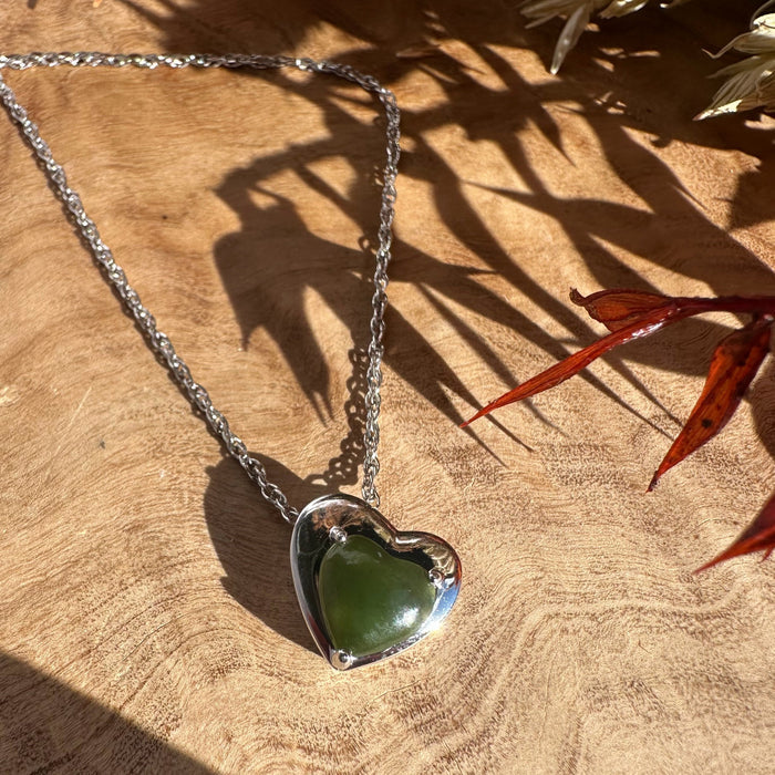 Silver heart pendant with green gemstone on a silver chain laid on a wooden surface.