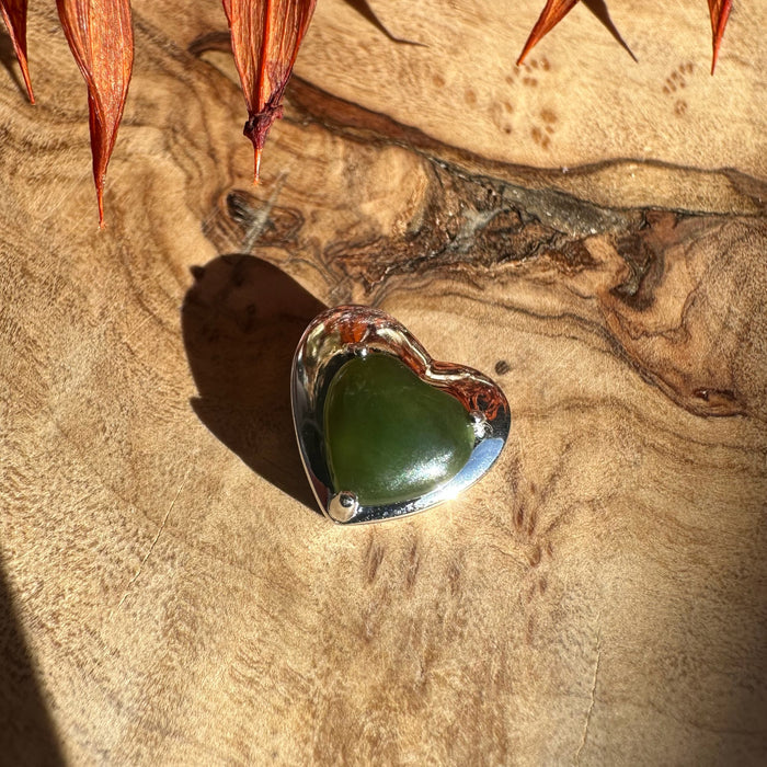 Green heart shaped gemstone set in a silver heart pendant on a wooden surface