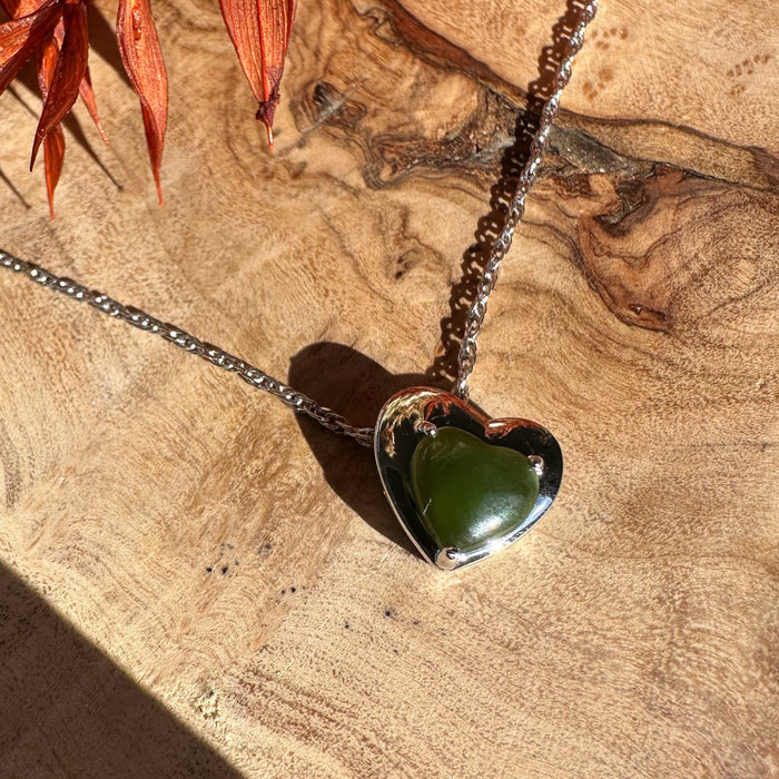 Silver heart pendant with green gemstone on a metal chain laid on wood