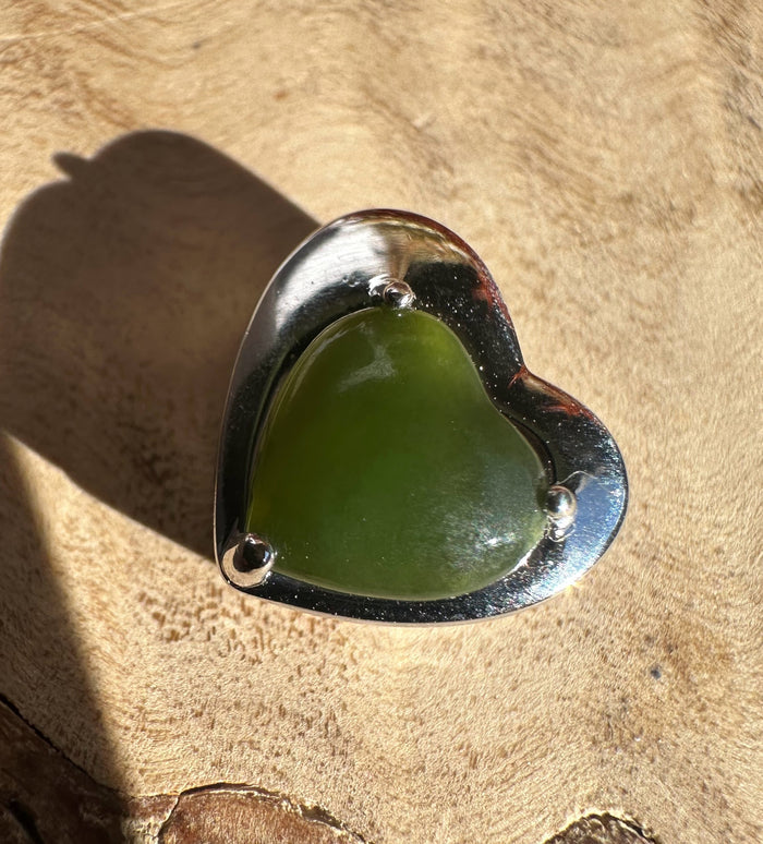 Top view of silver heart pendant with green heart shaped stone on a tan background