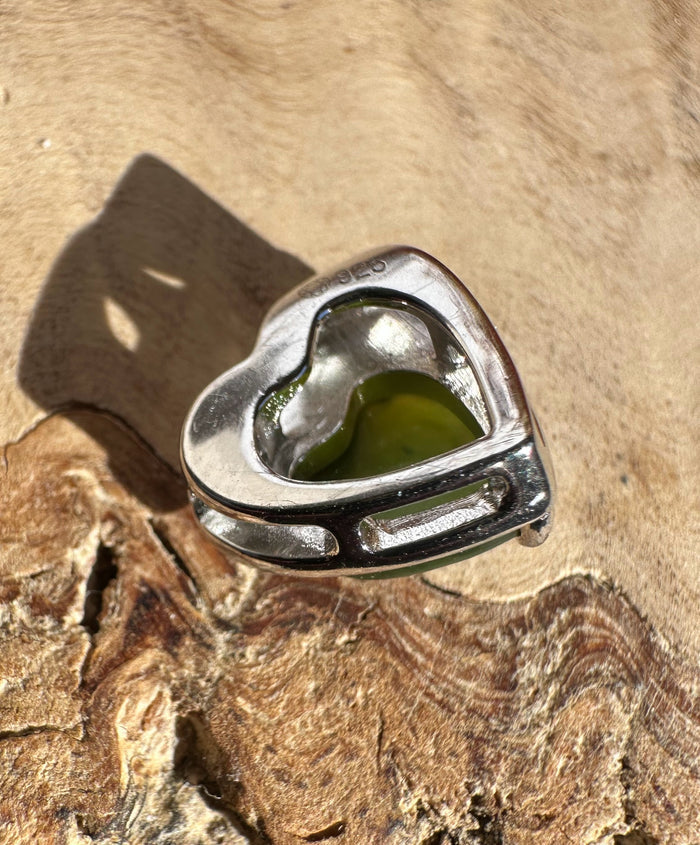 Silver heart pendant with a green inlay resting on a textured rock.
