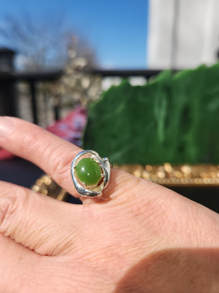 Silver Jade Ring with green jade cabochon worn on a finger outdoors with a bright blue sky and leaf backdrop