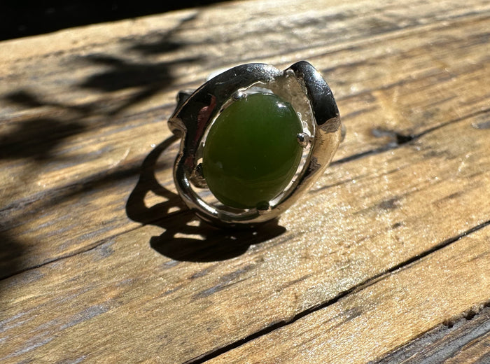 Silver ring featuring an oval green jade cabochon on a weathered wooden surface
