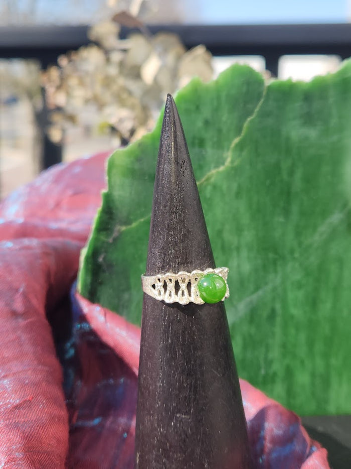 Silver Jade Ring with bright green jade on an intricate silver band shown on a dark cone against a green backdrop