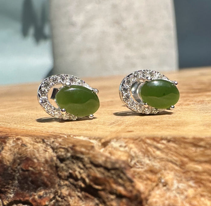 Pair of silver jade stud earrings with oval green jade stones and diamond halo settings.