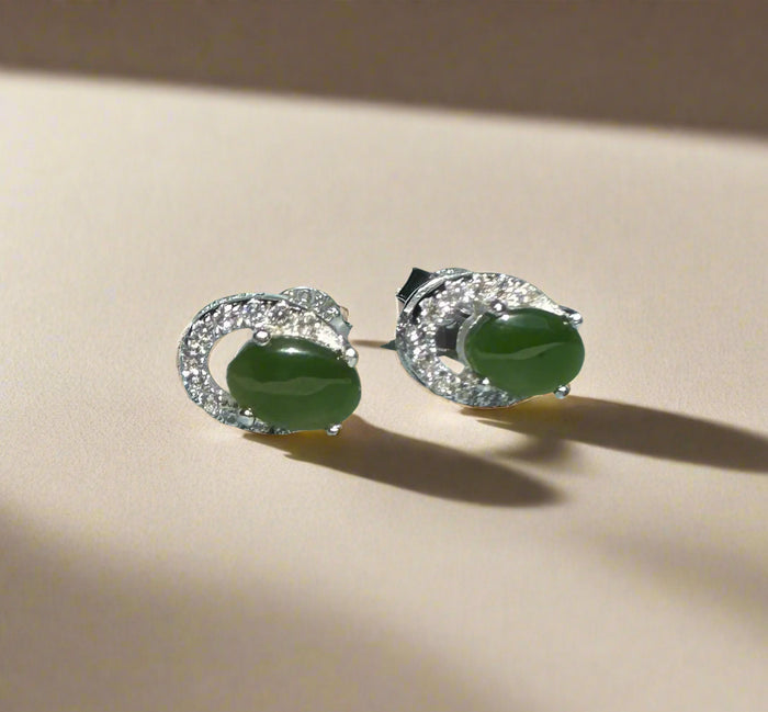 Pair of Silver Jade Studs with green oval centers and diamond halos resting on a light surface