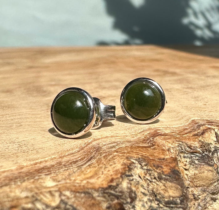 Front view of Silver Jade Studs with round green jade cabochons in silver bezels on a wooden surface