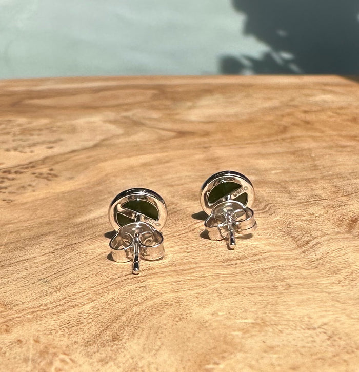 Round green jade stud earrings in a silver setting resting on a wooden surface