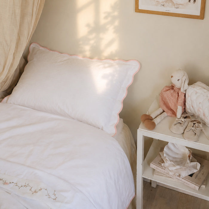 Bedroom with a bed featuring white bedding with Pink trim detail and a plush toy on a nightstand.