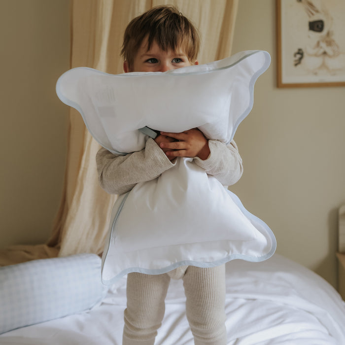 Child holding a toddler pillow with blue trim in a bedroom setting