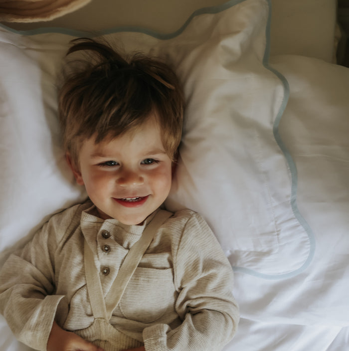Child lying on a bed with white toddler pillow with blue trim