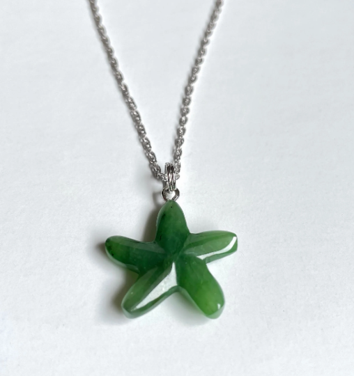 Bright green starfish jade charm on a silver chain against a light background