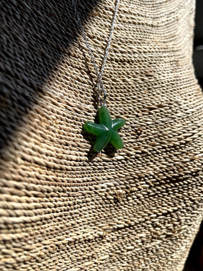 Green starfish charm necklace displayed on a woven surface
