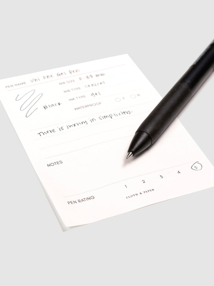 Uni One Gel Pen, 0.38 mm, Black Ink, Black Barrel, Cloth and Paper. Close up on pen nib resting on pen test sheet.