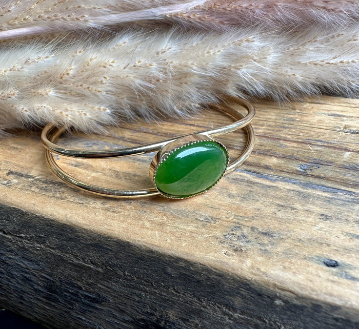 Vintage gold-tone bracelet with oval green jade on a wooden surface lined with dried grasses