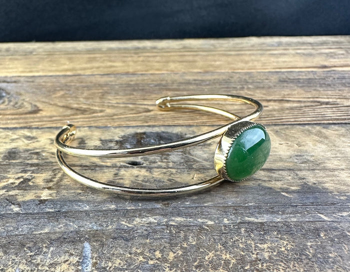 Vintage gold cuff bracelet with a green jade cabochon set in a decorative bezel on a weathered wooden surface